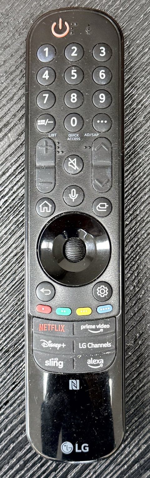 The TV's remote, a long black remote with number keys, volume and channel rockers, a mic button between them, a scroll wheel, and app shortcut buttons near the bottom.